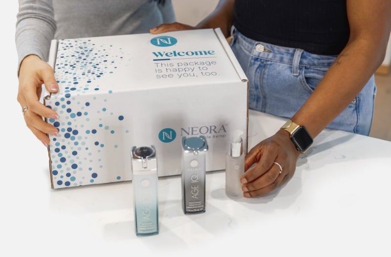 Dos personas abriendo la Neora Welcome Box y productos Neora alrededor de la caja.